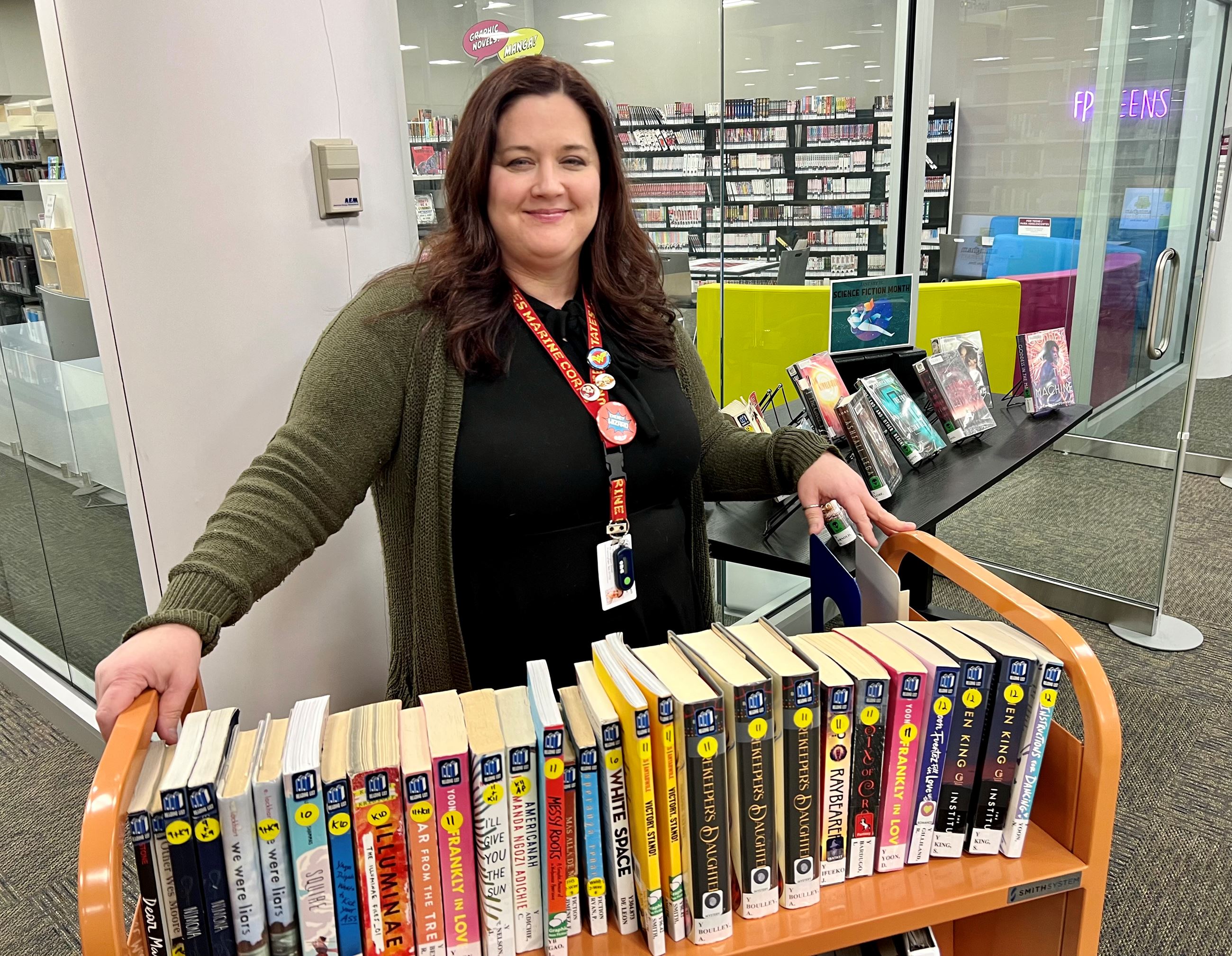Photo of Dawn Dellasanta in front of cart of books in library
